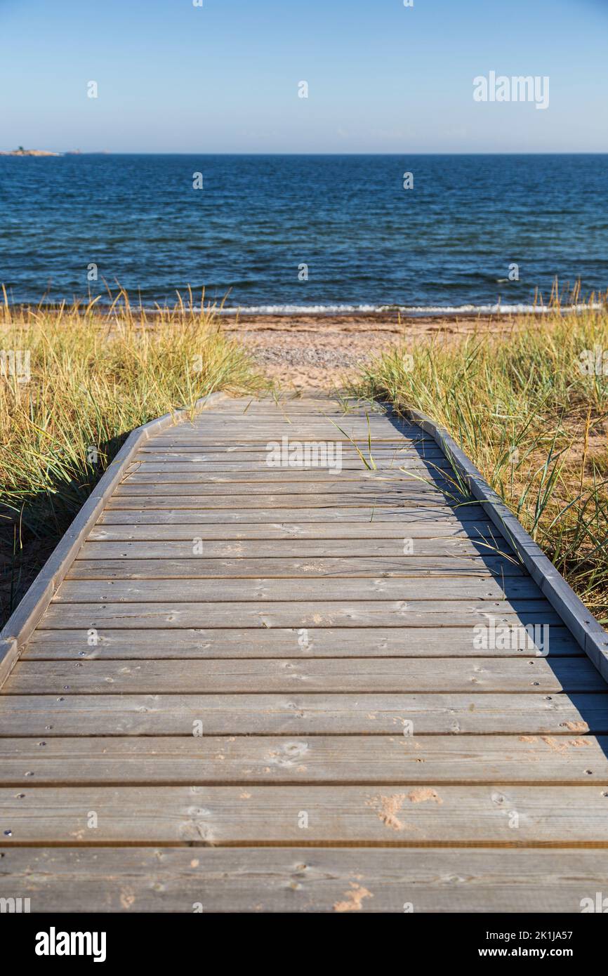 Wooden boardwalk leading to an empty beach in Hanko, Finland, on a sunny day in the summer. Focus on the front, shallow depth of field. Stock Photo