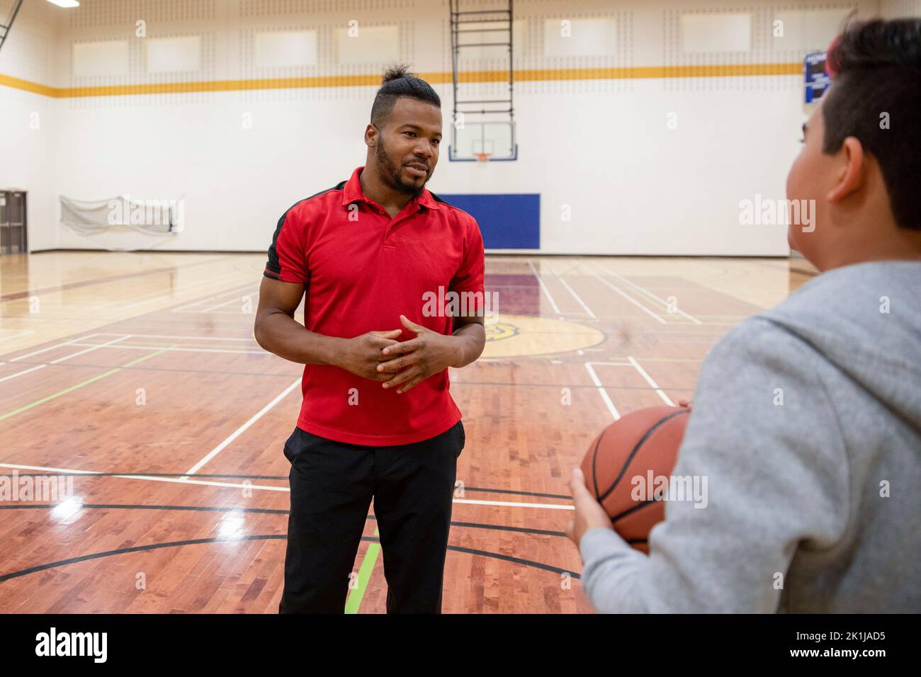 Junior high basketball coach talking to student in gymnasium Stock