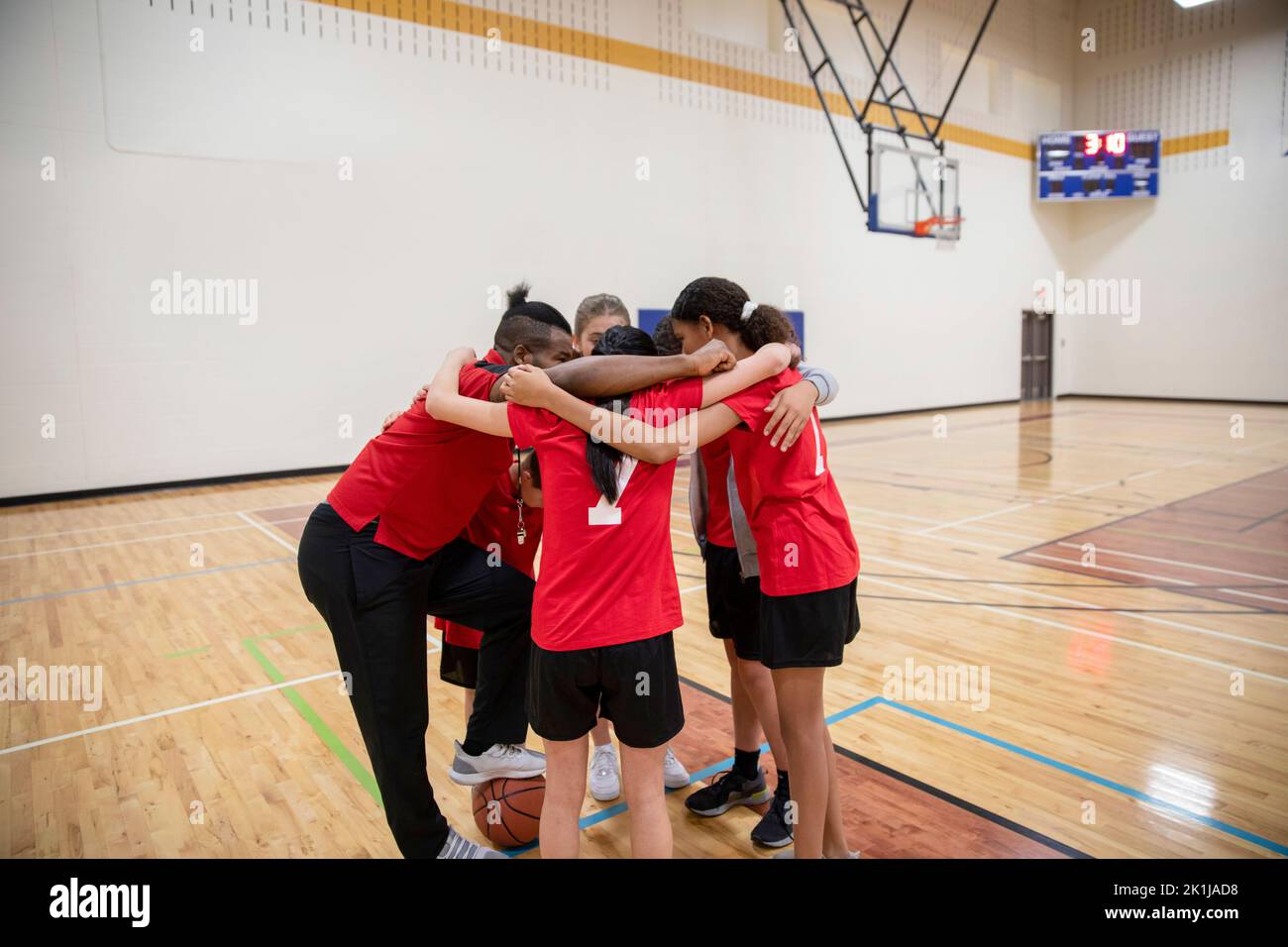 Junior high basketball coach and team in huddle in gymnasium Stock