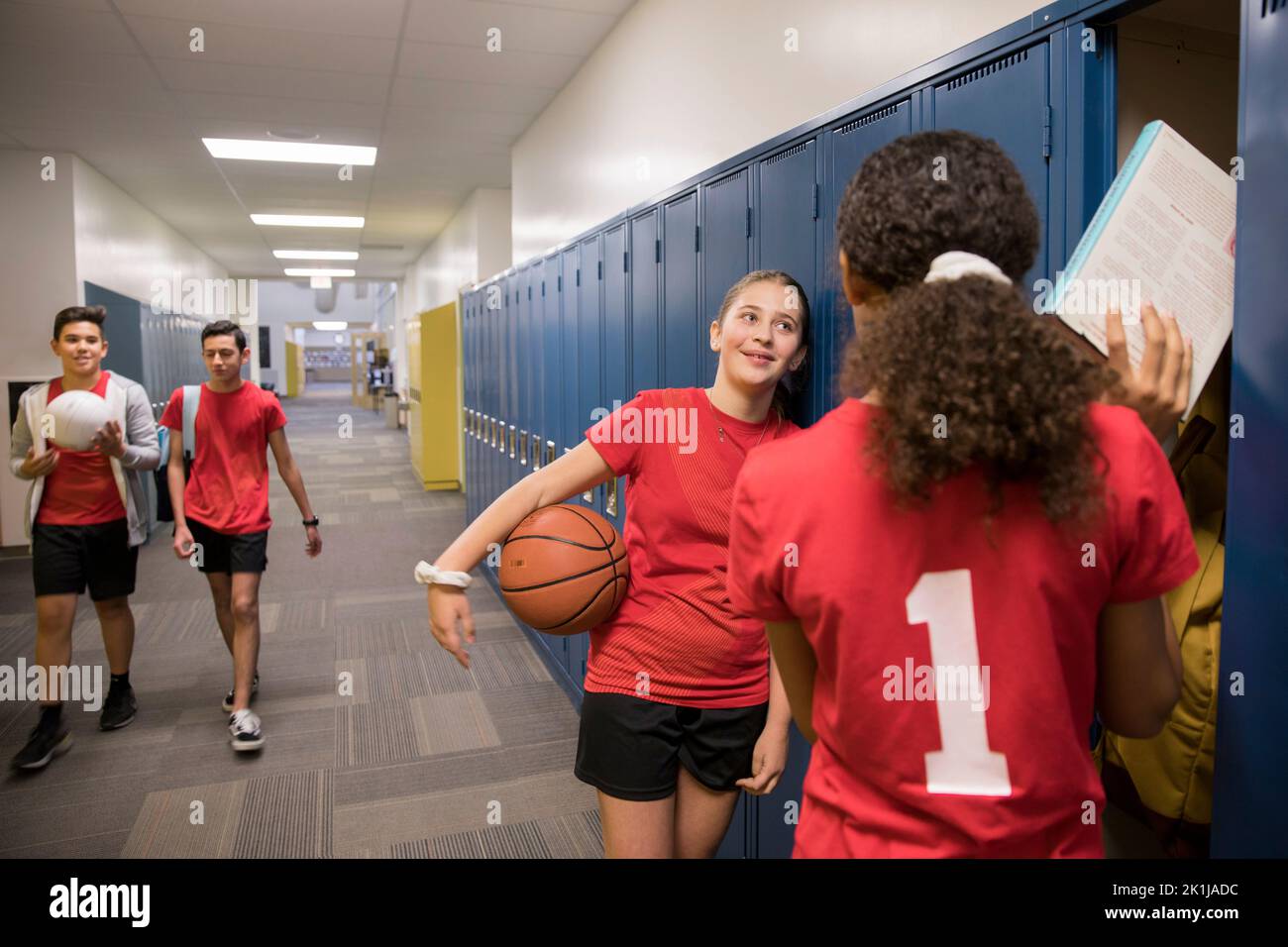 Junior high girl basketball players talking at lockers in corridor