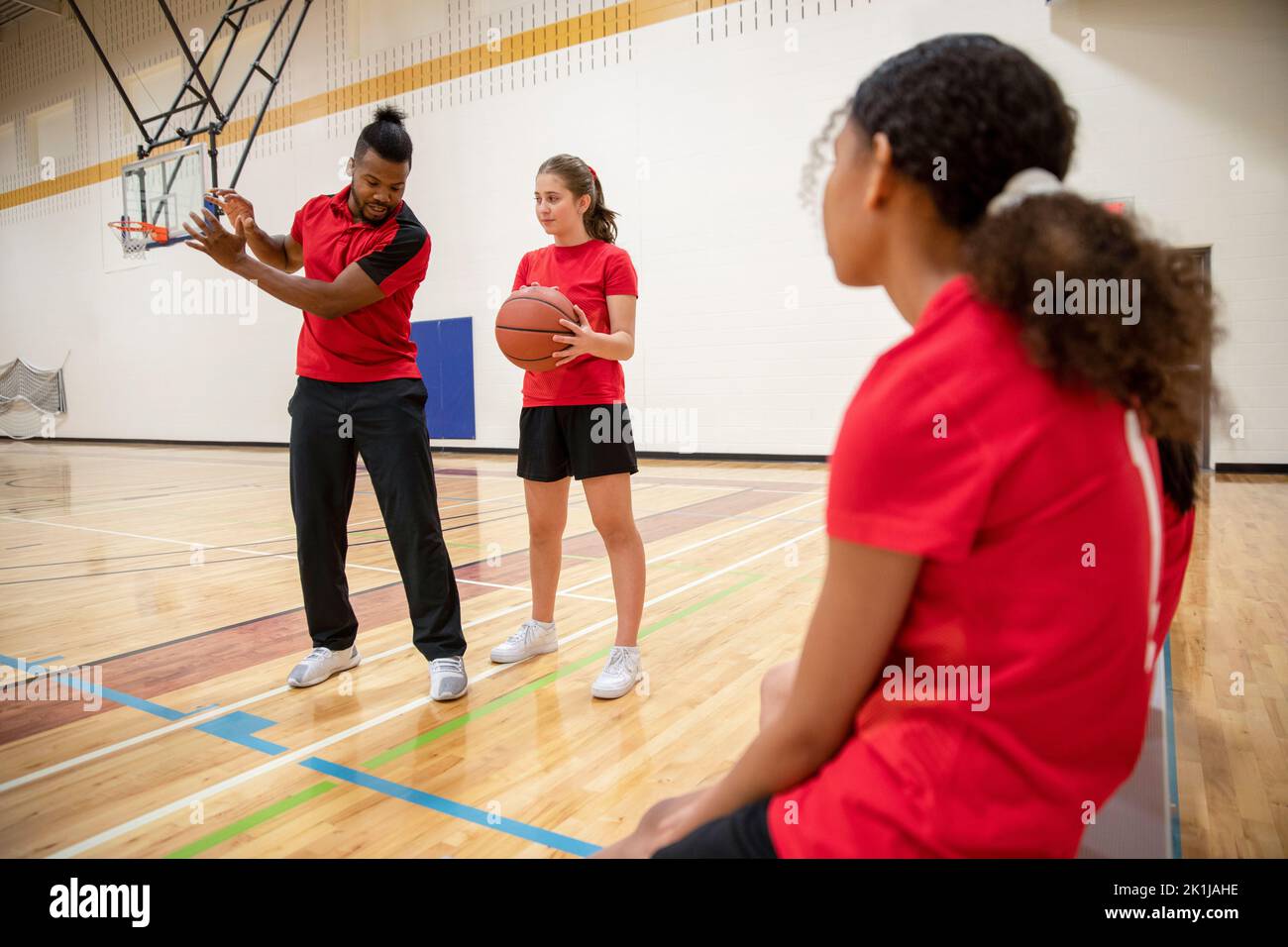 Junior high basketball coach and student practicing in gymnasium Stock