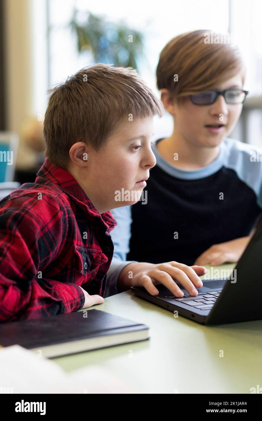 Junior high boy with Down Syndrome using laptop with classmate Stock