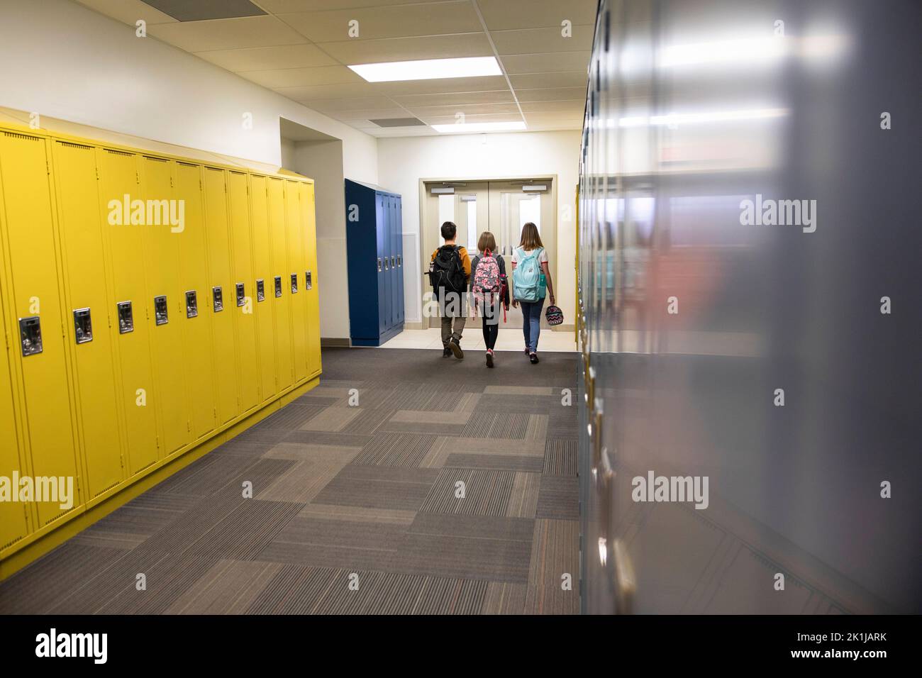 Junior high students with backpacks walking in corridor with lockers