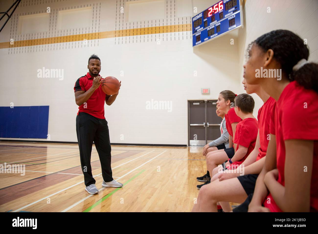 Junior high students listening to basketball coach in gymnasium Stock