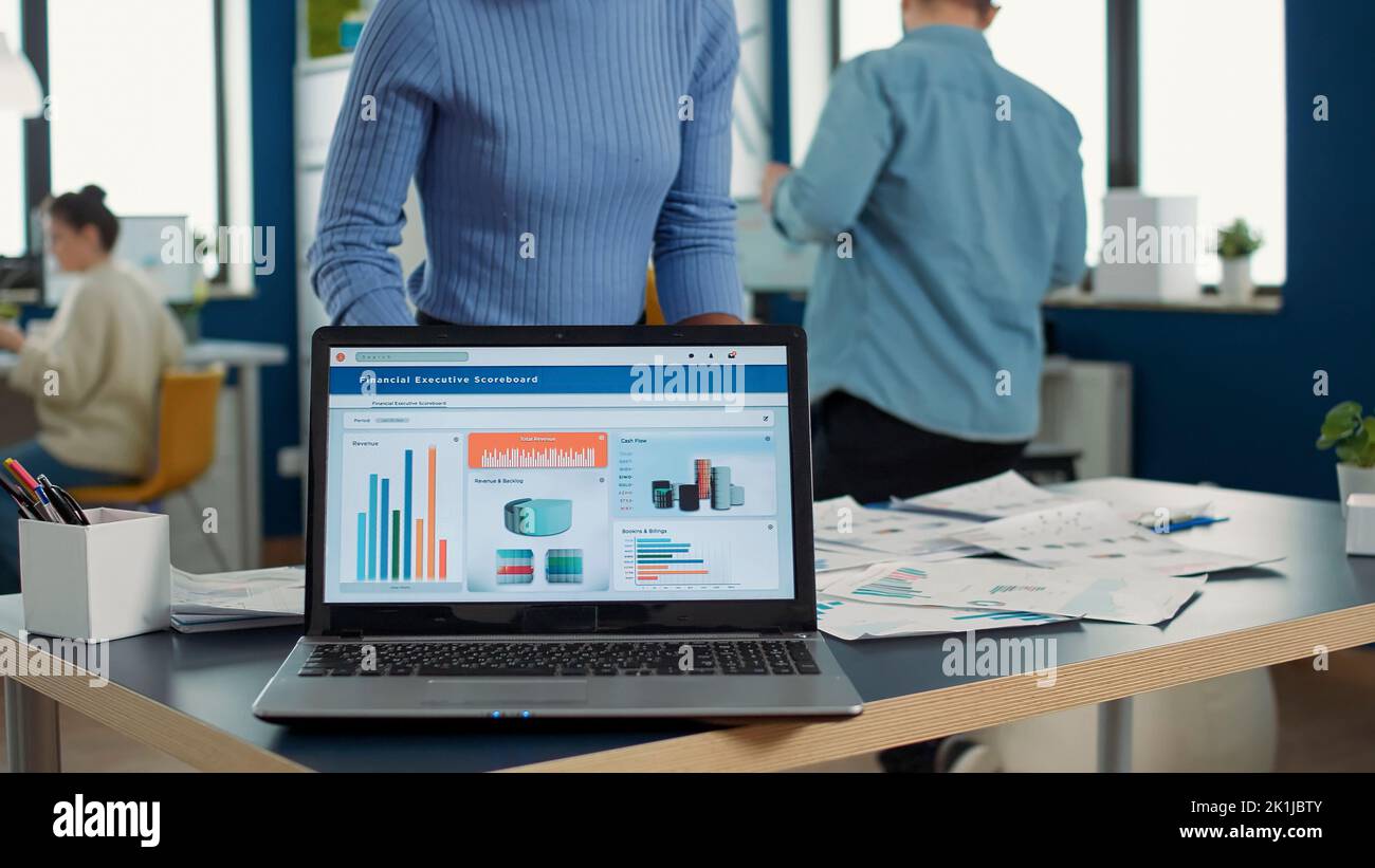 Closeup of laptop screen showing moving charts and financial statistics on desk in busy startup office. Selective focus on portable computer with business management software and performance indicators. Stock Photo