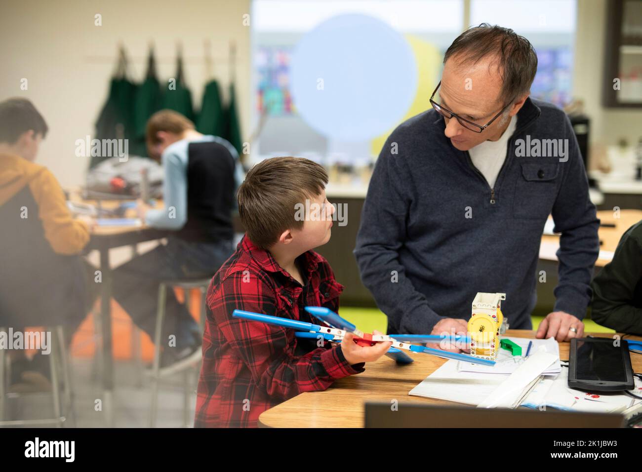Male junior high teacher helping student with Down Syndrome assembling