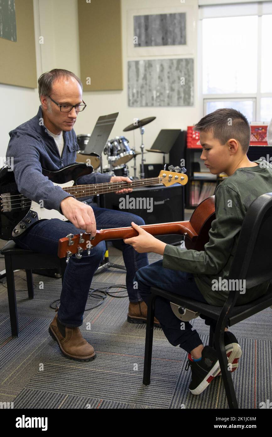 Junior high music teacher guiding student playing guitar in classroom