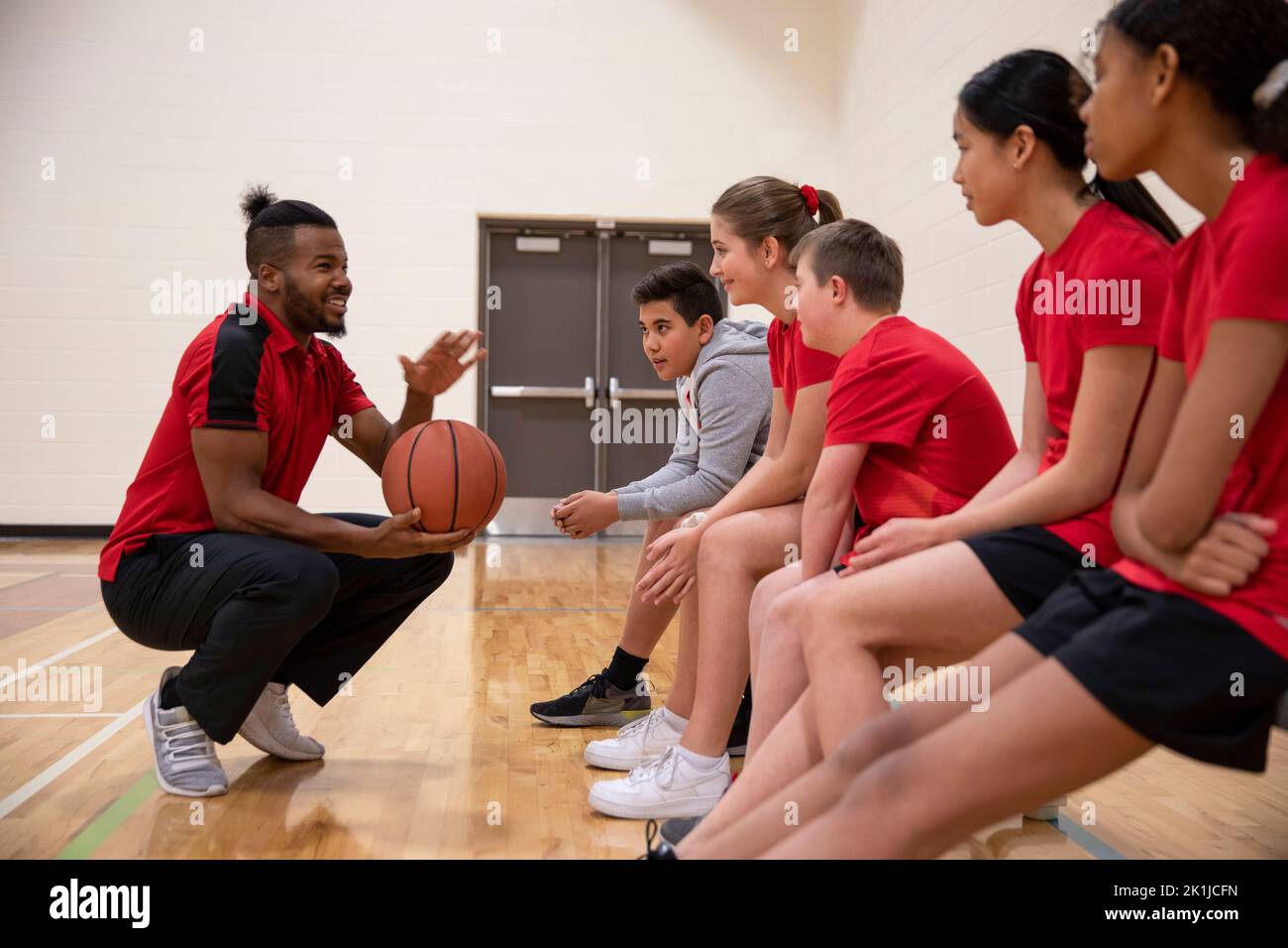 Junior high basketball coach talking to students on bench in gymnasium
