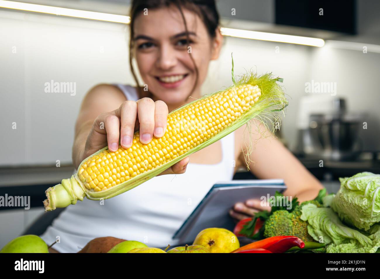 Corn Notepad A young woman in the kitchen with a notepad and corn in her hand Stock ...