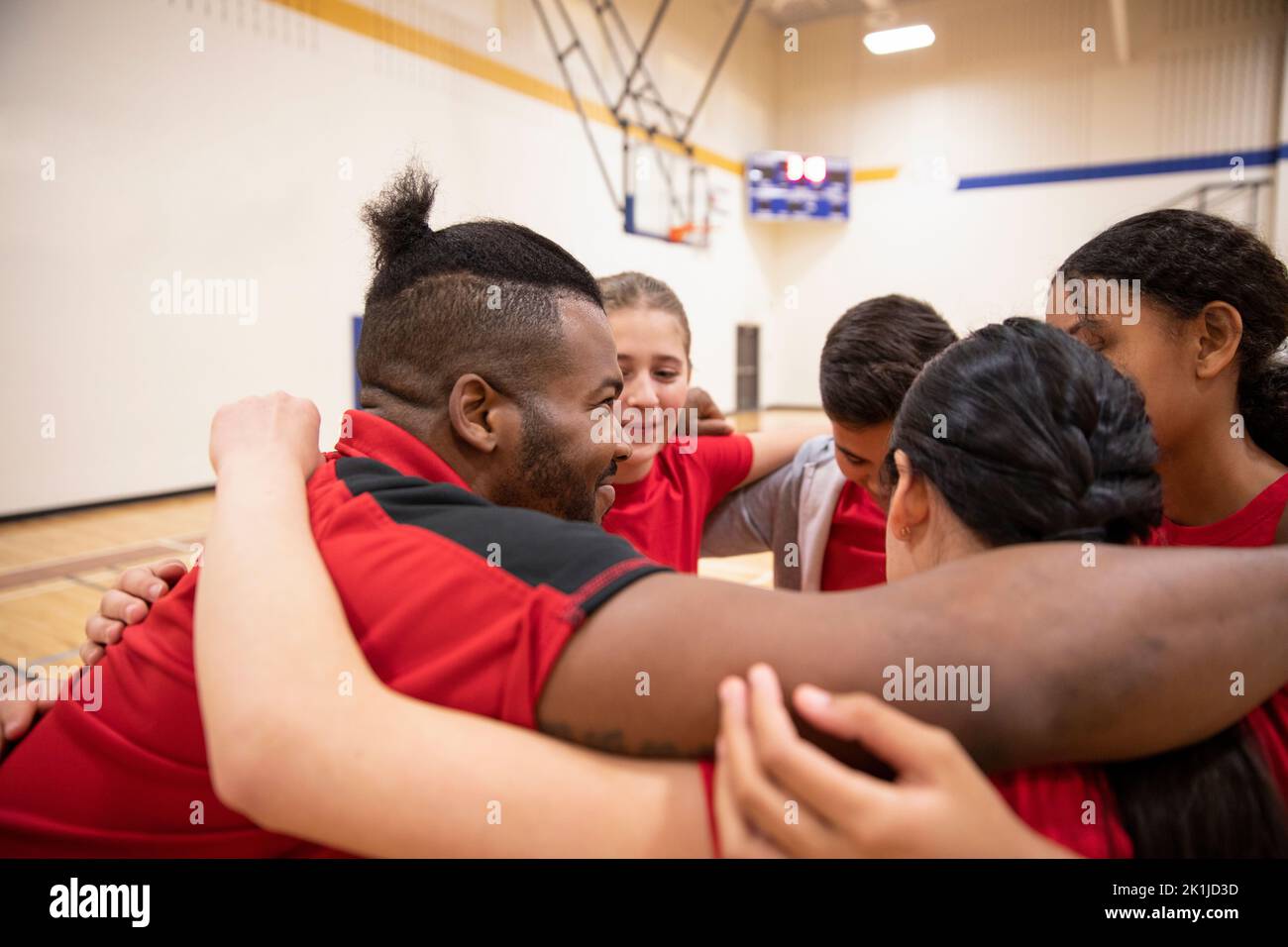 Junior high basketball coach and students in huddle in gymnasium Stock