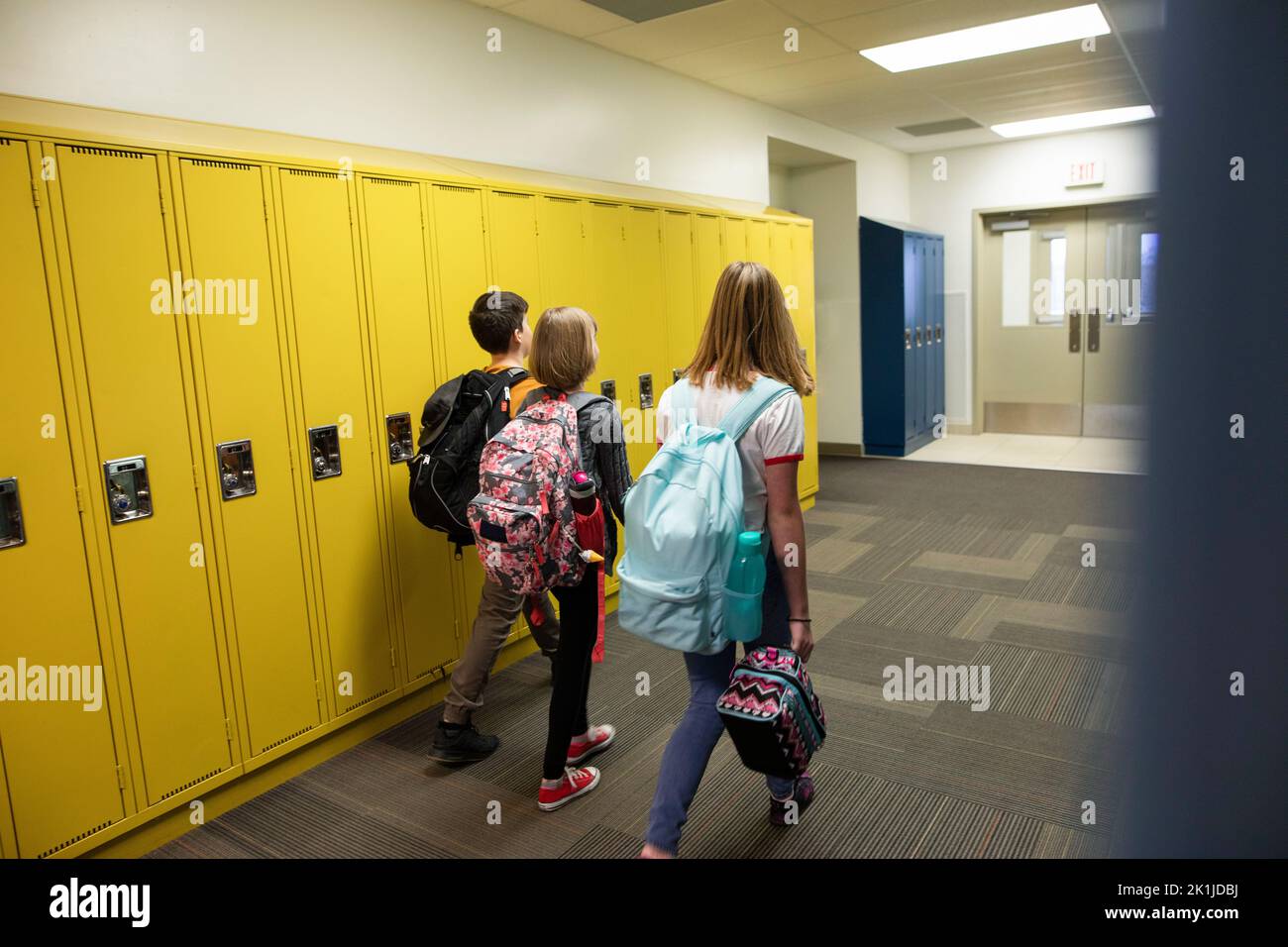 Junior high students with backpacks walking along lockers in corridor