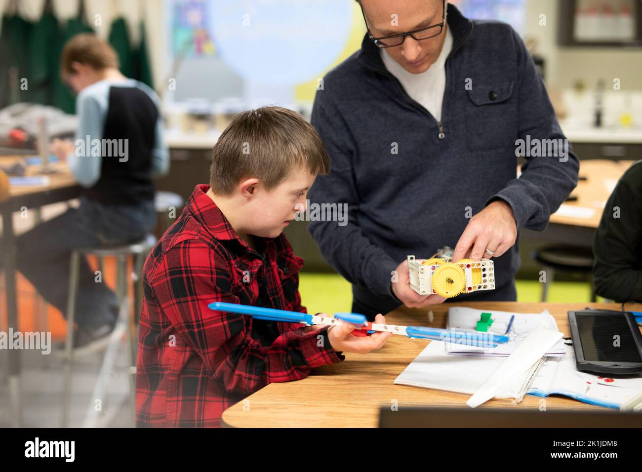 Male junior high teacher helping student with Down Syndrome assembling