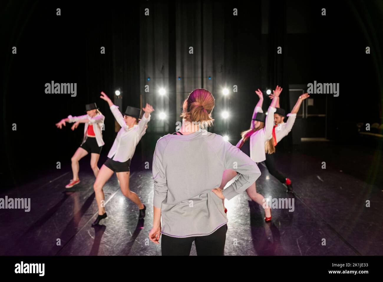 Female dance instructor watching jazz dancers rehearse on stage Stock