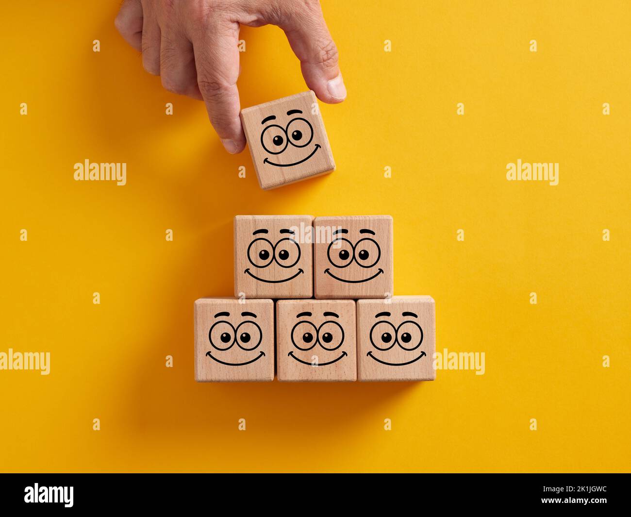 Hand placing wooden cubes with smiling face emoticons arranged in pyramid staircase. Positive attitude, customer satisfaction, emotional management or Stock Photo