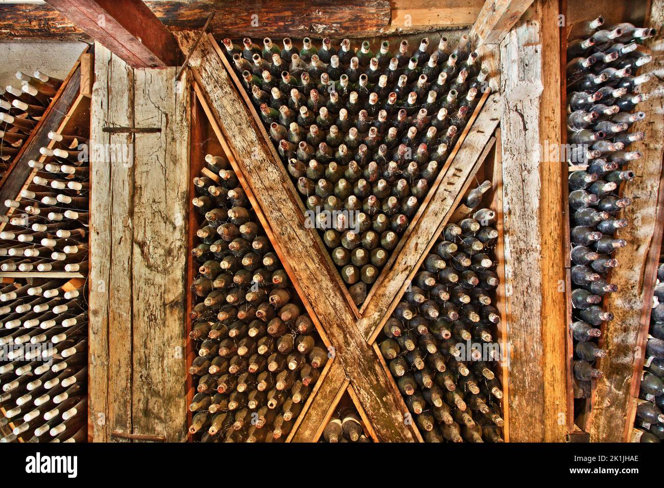 Old wine cellar with wooden beams and dozens of old, dusty bottles of wine, maturing peacefully in a cellar somewhere in Zakynthos island, Greece Stock Photo