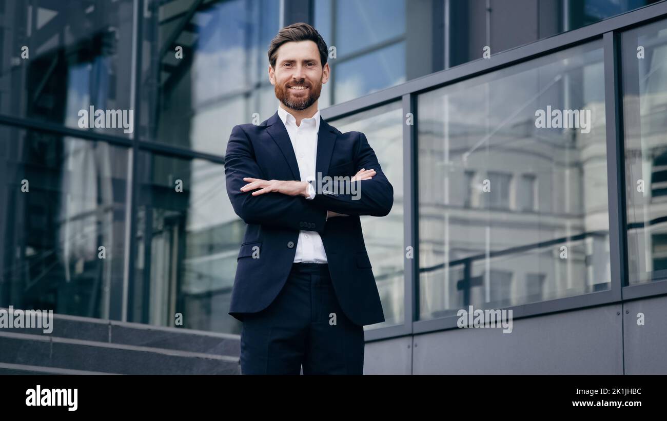 Successful confident caucasian bearded businessman in suit standing outdoors on background office building smiling proud male professional worker Stock Photo