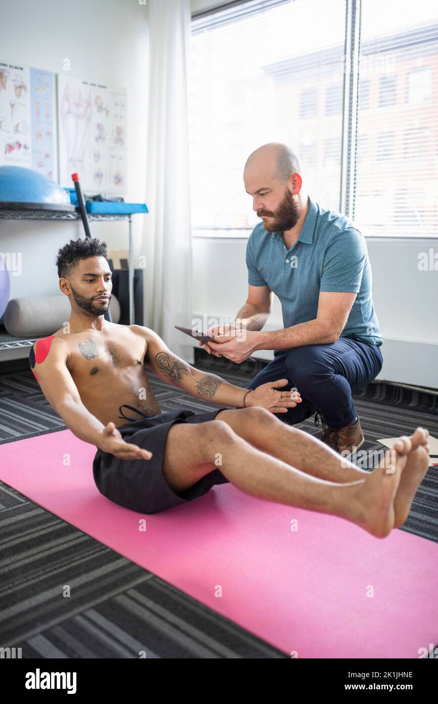Physiotherapist using digital tablet to help client exercise Stock Photo