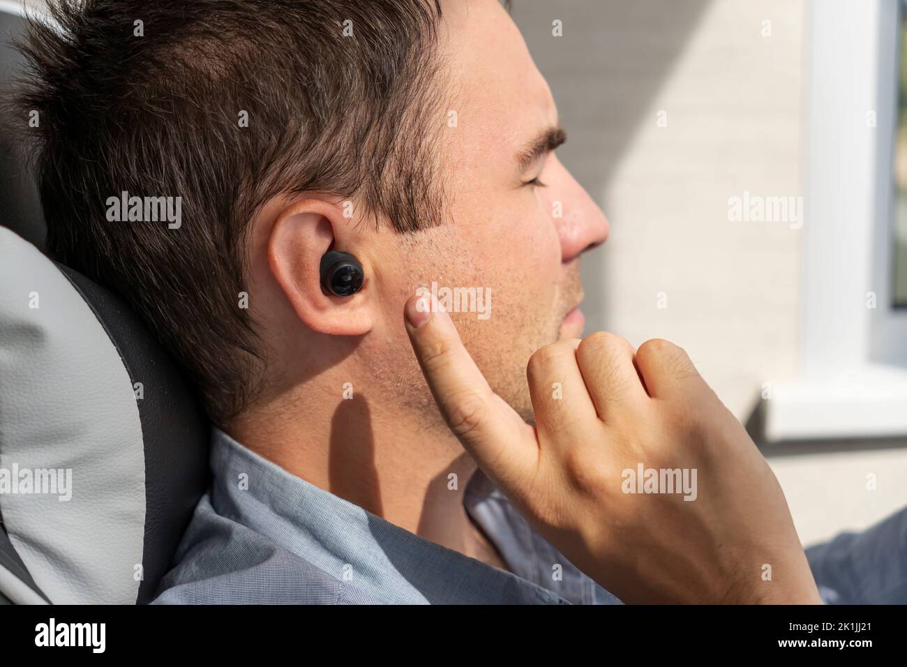 Close-up of wireless earphone in human ear on dark background. insert the earphone into the ear. listening to music with headphones. Stock Photo