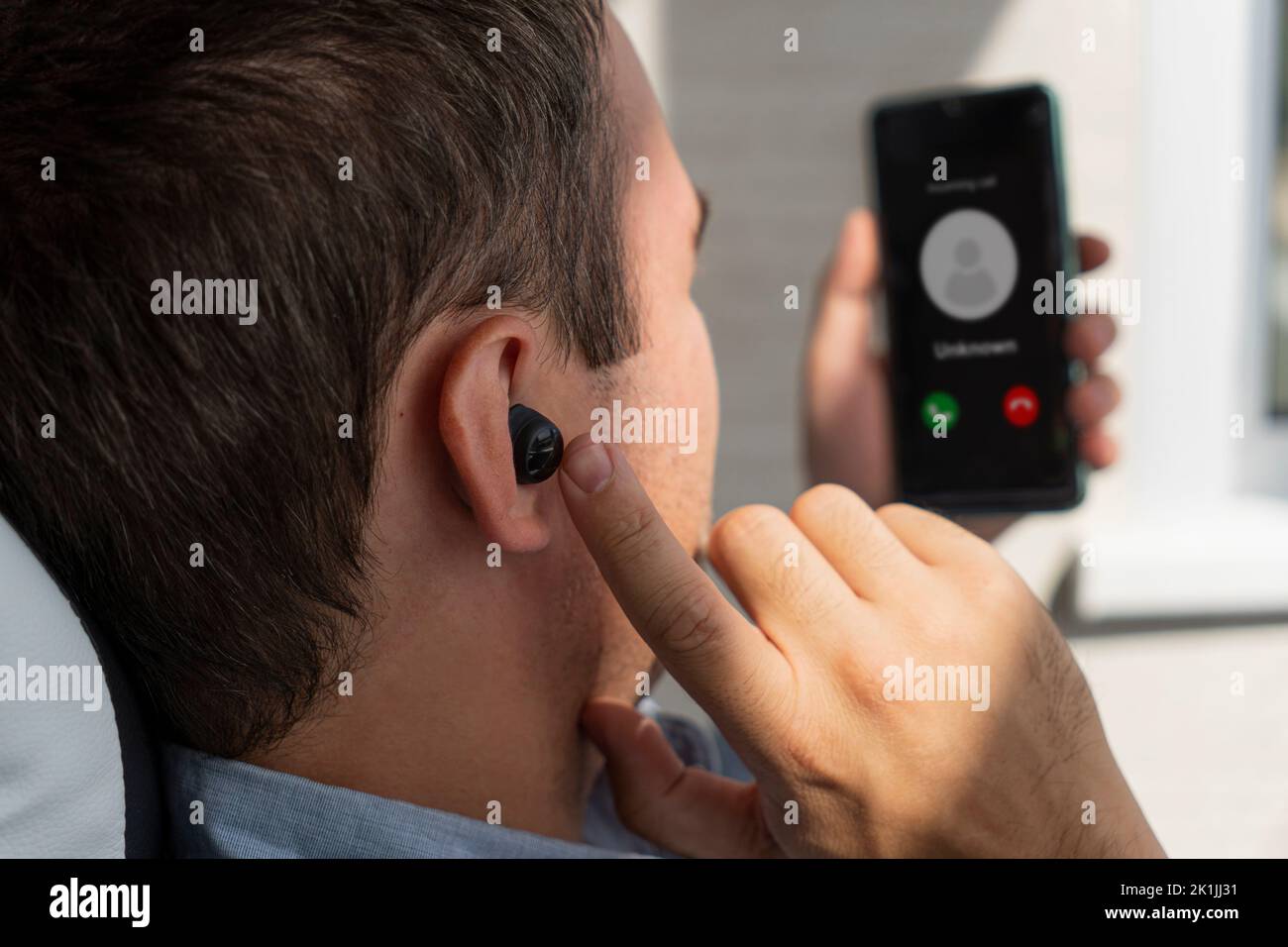 a young businessman man receives an incoming call on a smartphone using a wireless earphone Stock Photo