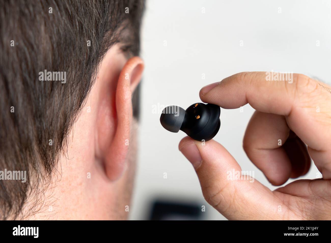 the small black earphones inserted into the ear of men close up. insert the earphone into the ear Stock Photo