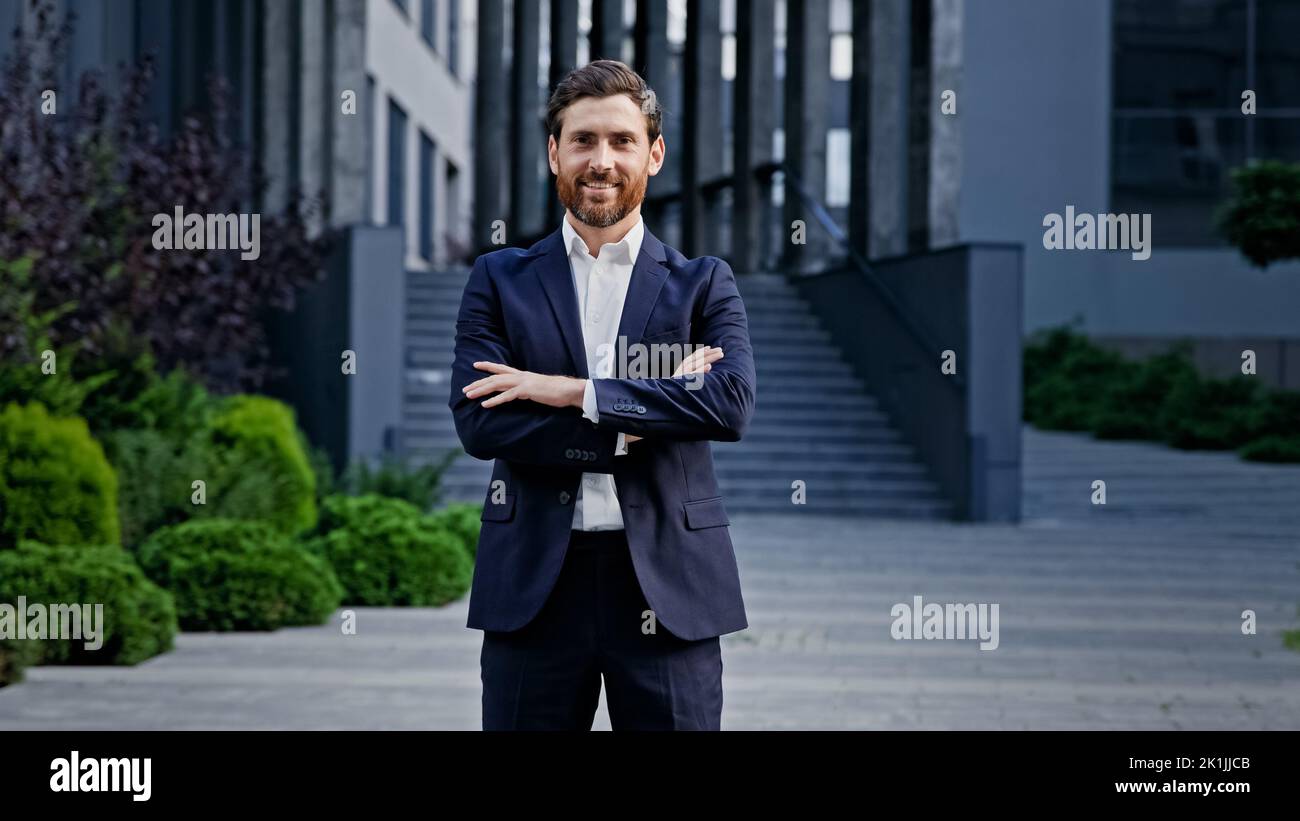 Stylish man in suit on street confident leader posing with crossed arms outdoors handsome successful male professional manager smiling looking at Stock Photo