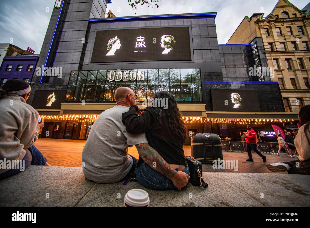 London, UK. 18th Sep, 2022. A couple sit outside a cinema building in Leicester Square, London, Britain, where portraits of the late Queen Elizabeth II are displayed on large screens, on September 18, 2022. Credit: Roman Vondrous/CTK Photo/Alamy Live News Stock Photo