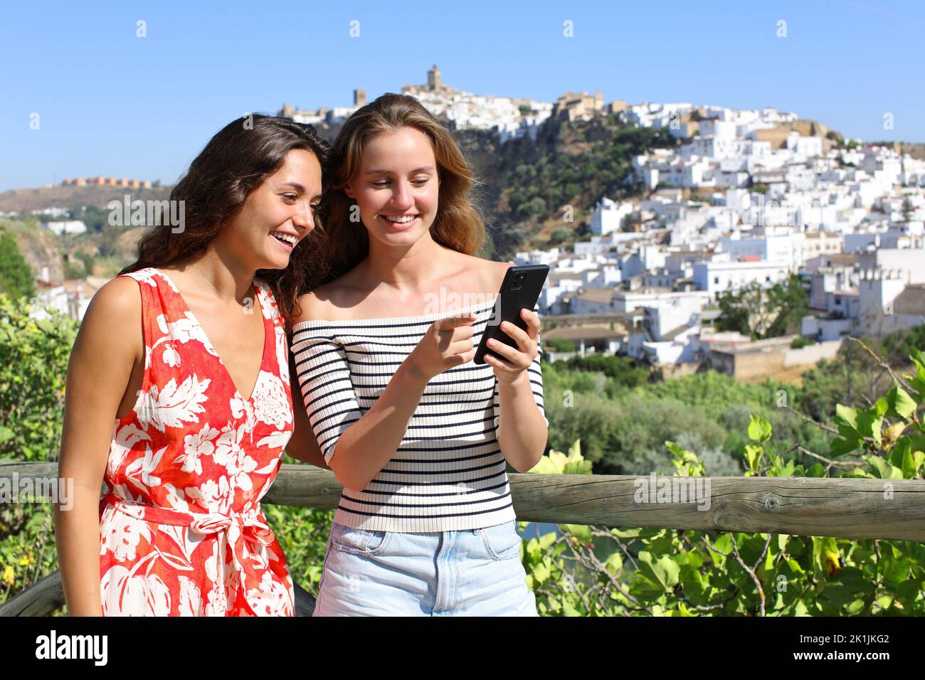 Two happy tourists checking smart phone on summer vacation outdoors Stock Photo