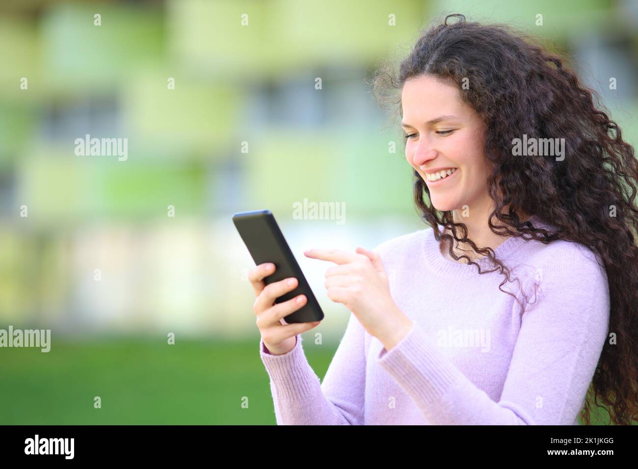 Happy woman with curly hair walks checking smart phone content in the street Stock Photo