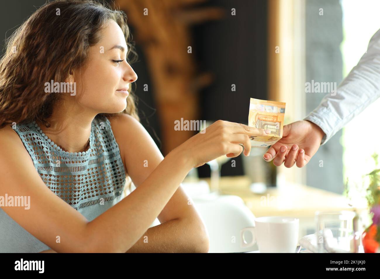 Woman in a restaurant paying to a waiter with a paper bill Stock Photo
