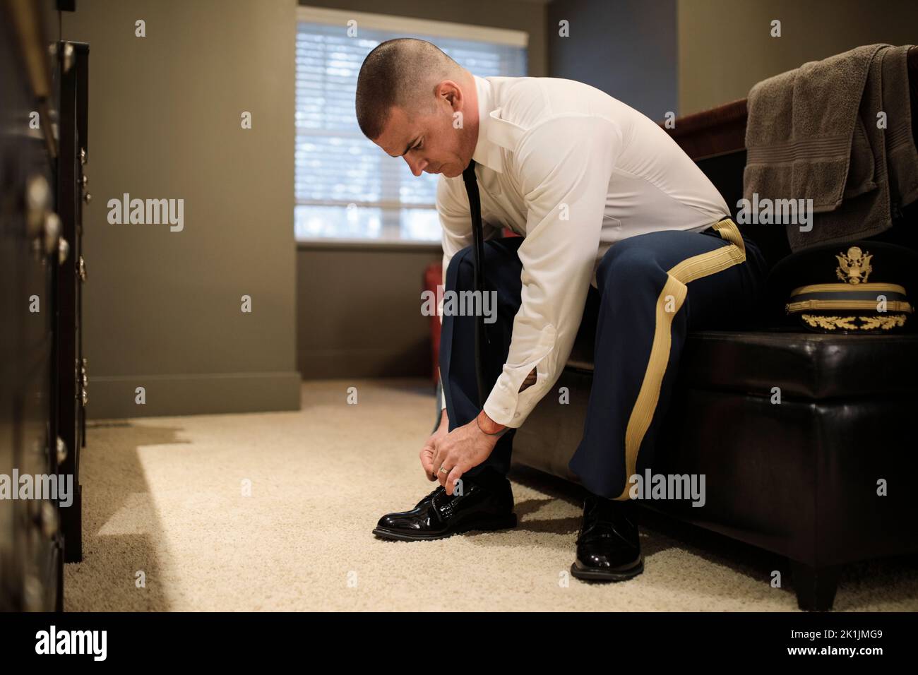 Male soldier putting on military dress uniform tying shoe in bedroom Stock Photo