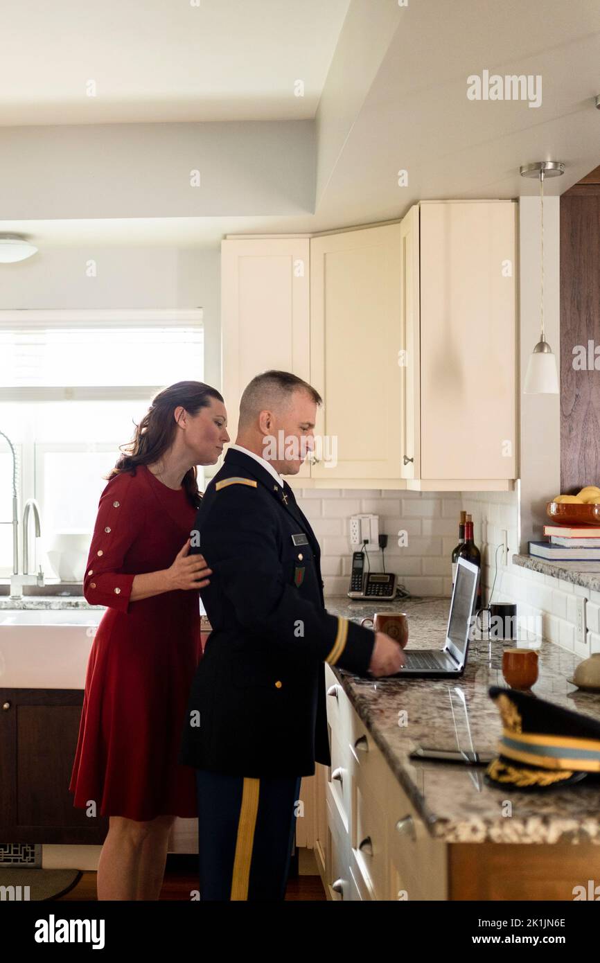 Wife watching husband in military dress uniform use laptop in kitchen Stock Photo