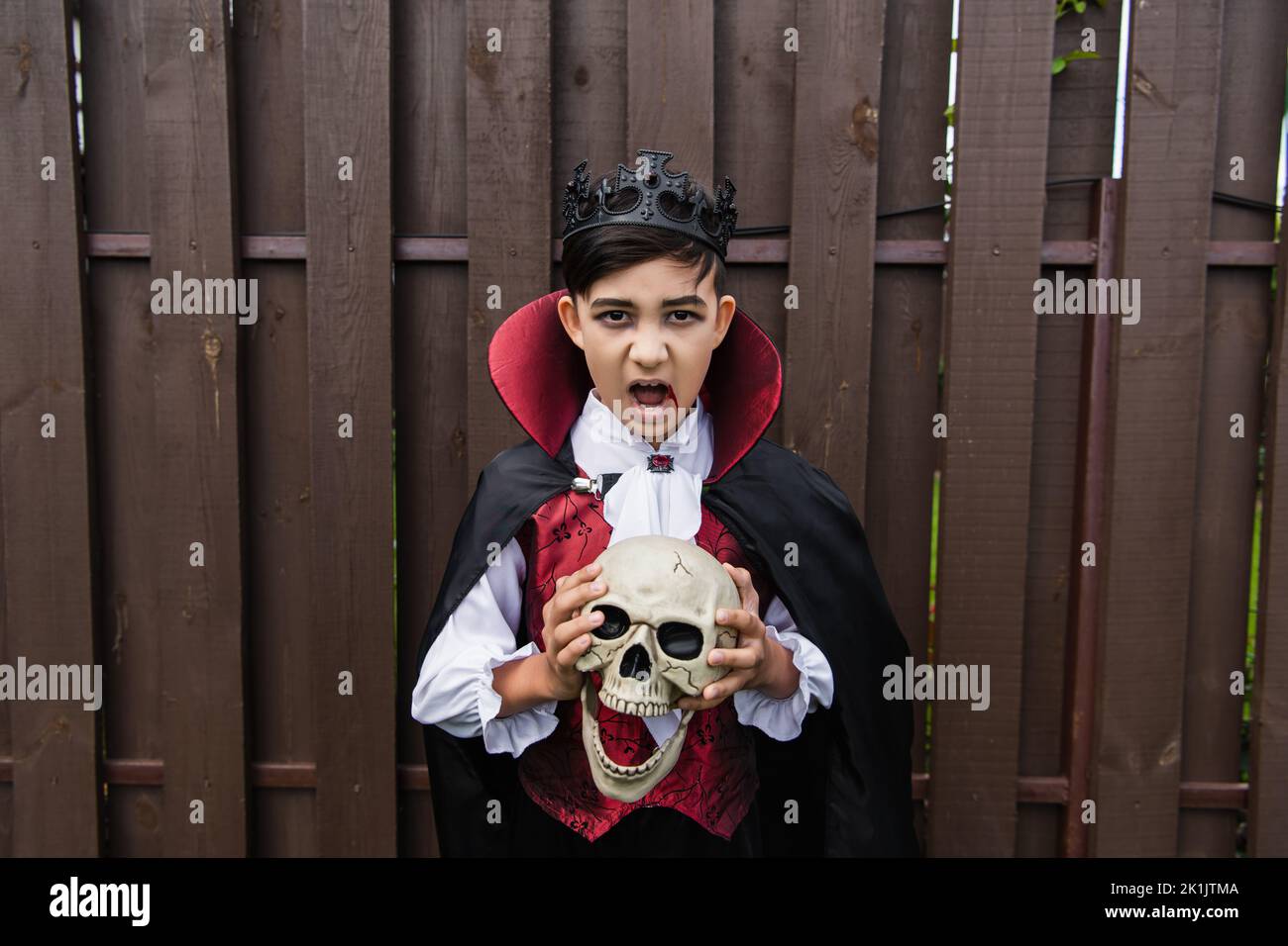 asian boy in vampire costume holding skull and screaming while looking at camera Stock Photo