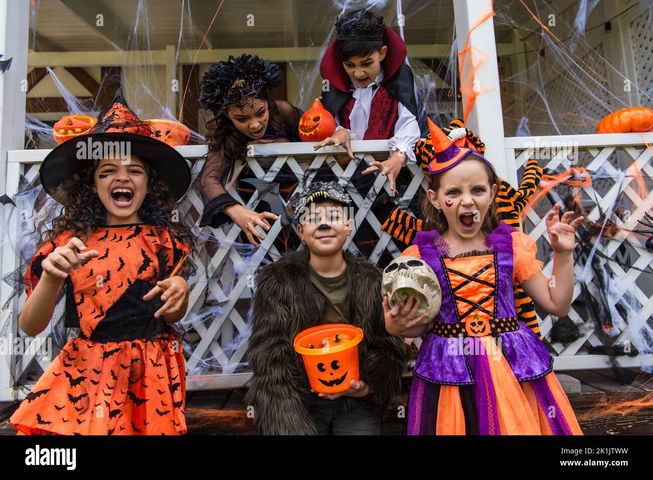 Girls in halloween costumes grimacing at camera near multiethnic friends outdoors Stock Photo