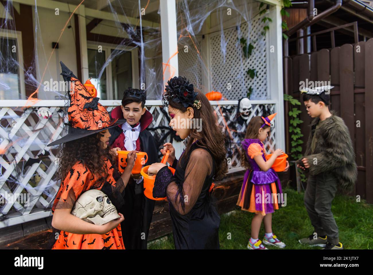 Preteen girls in halloween costumes holding skull and bucket near