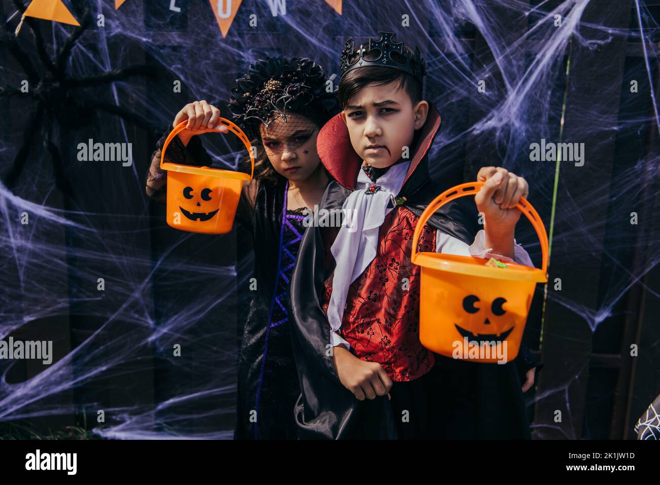 Serious multiethnic kids in halloween costumes holding buckets near