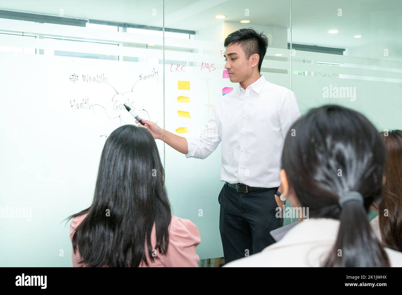 Trainer, Asian ethnicity giving a presentation on the white glass board to an audience. Stock Photo