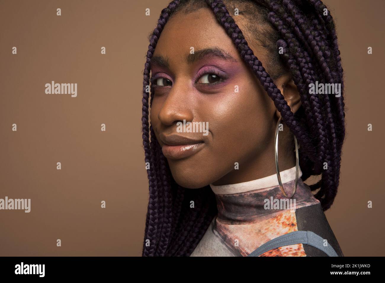 Portrait of confident young woman with purple eyeshadow and braids Stock Photo