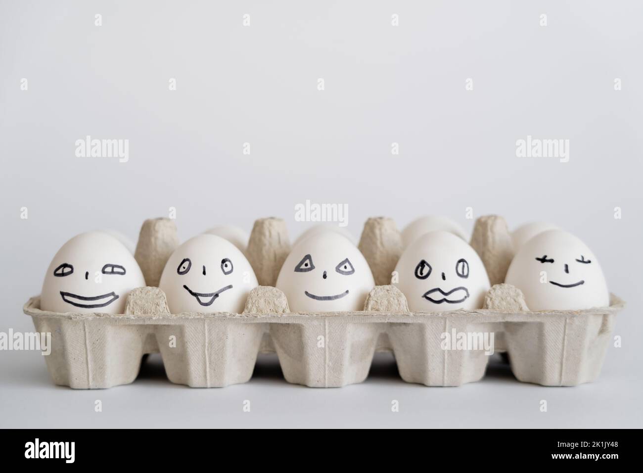 Painted chicken eggs with facial expressions in tray on white background Stock Photo