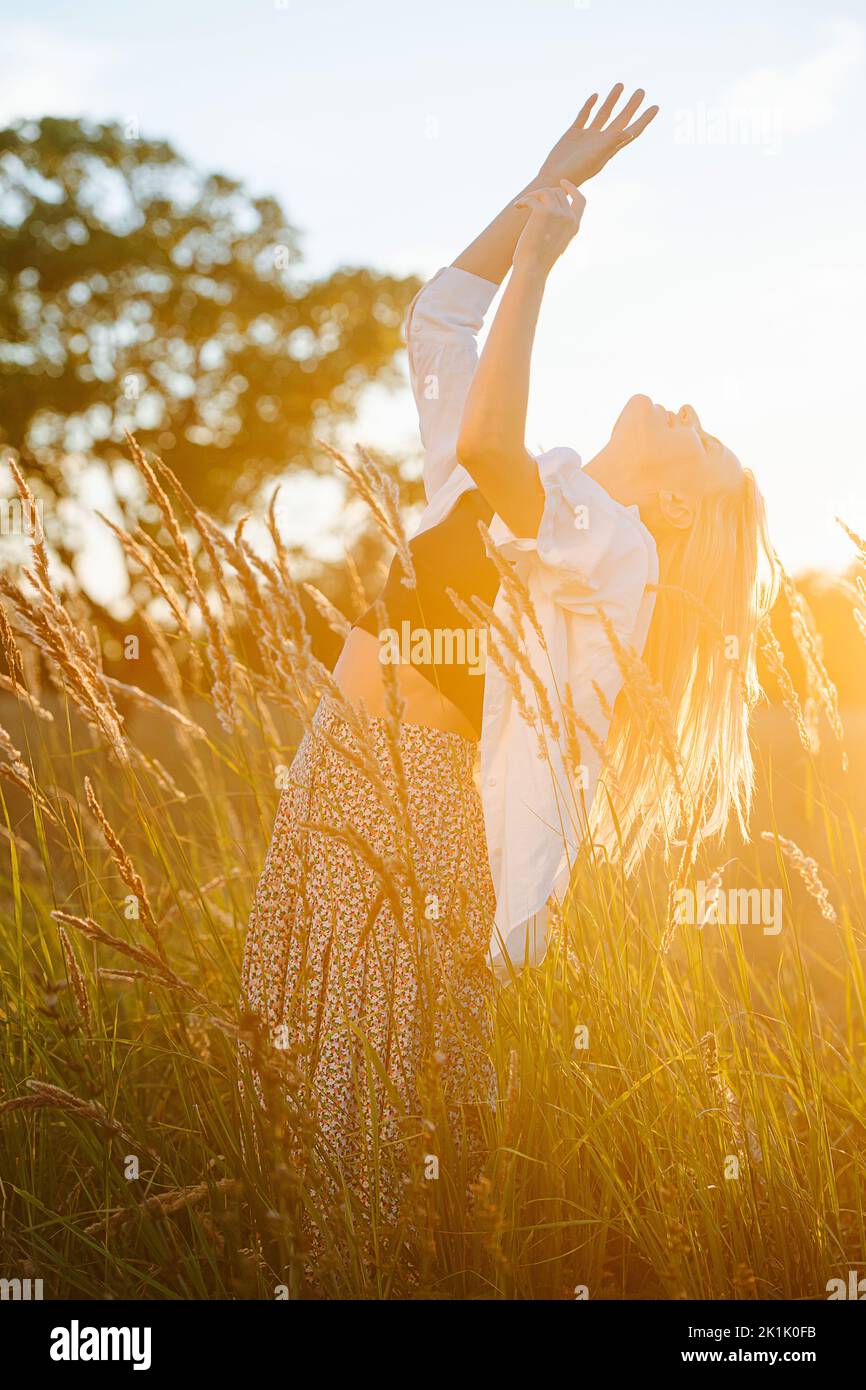 Bathing in the sun young blond woman standing amidst wheat field. Stock Photo