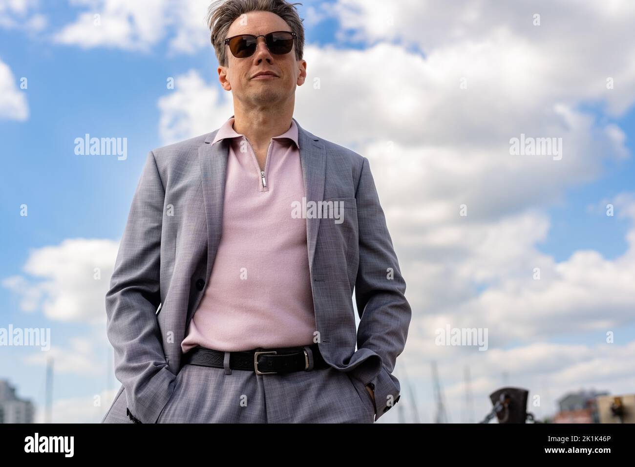 A handsome businessman in a casual grey suit in front of a busy marina with luxury yachts moored up Stock Photo