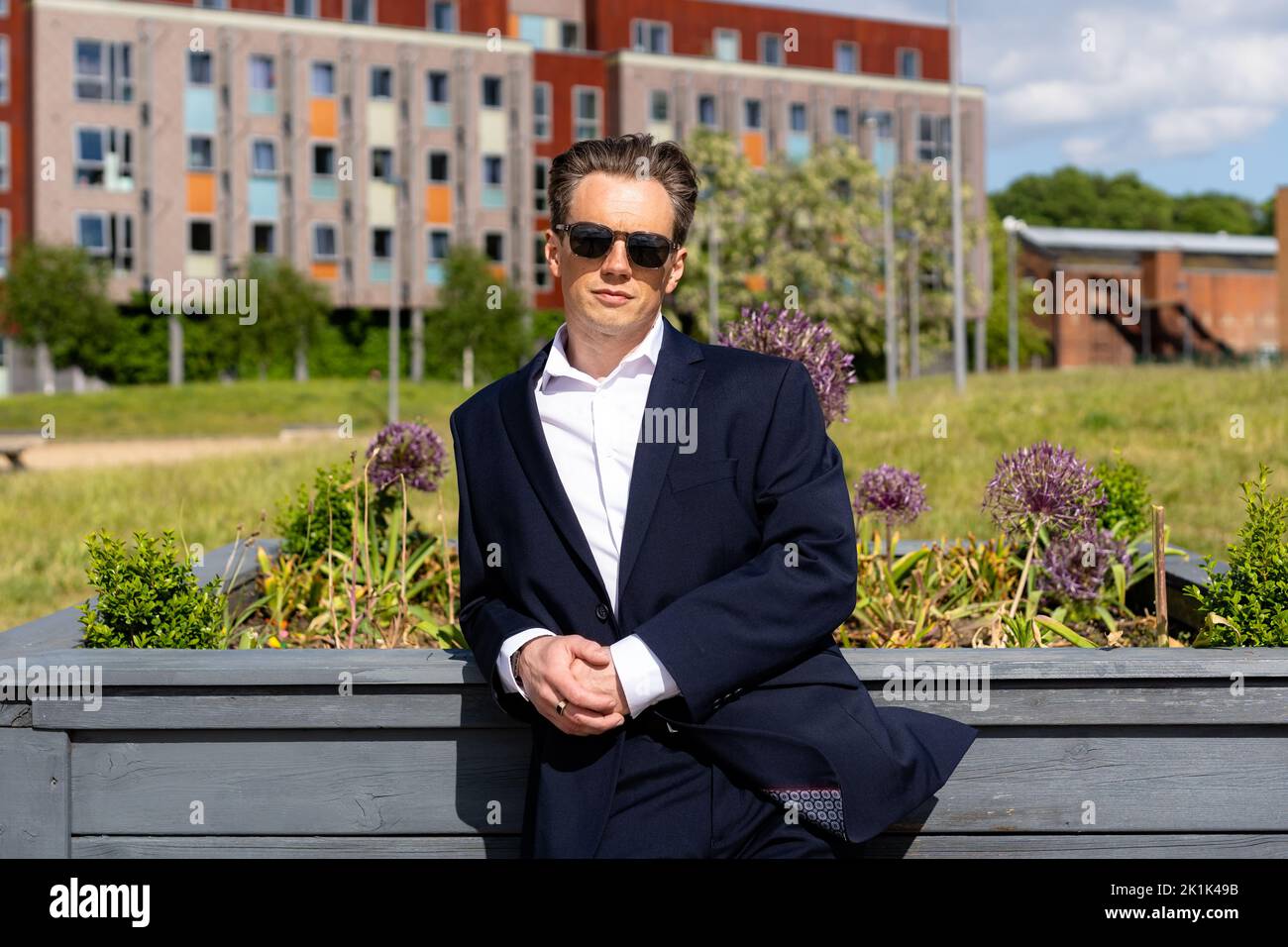 A handsome businessman in a casual dark blue suit in front of a residential area Stock Photo