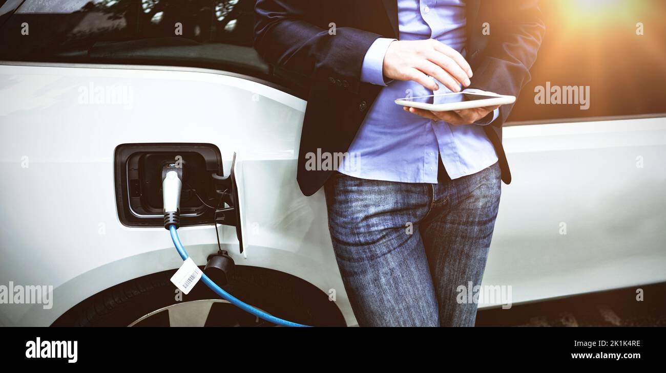 Businessman using digital tablet while charging electric car at charging station Stock Photo