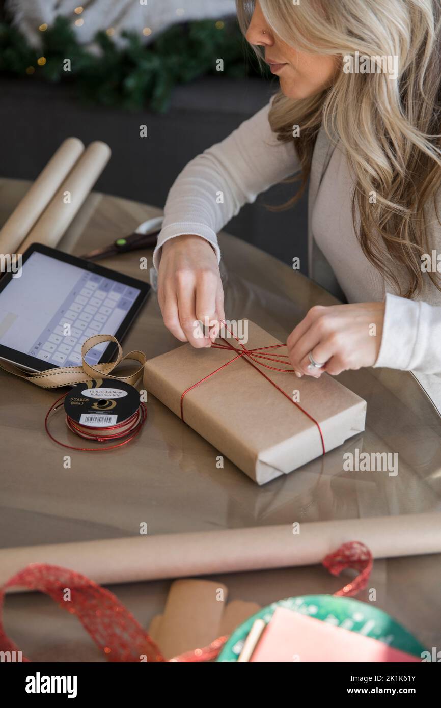 Woman wrapping Christmas gifts using tutorial on digital tablet Stock