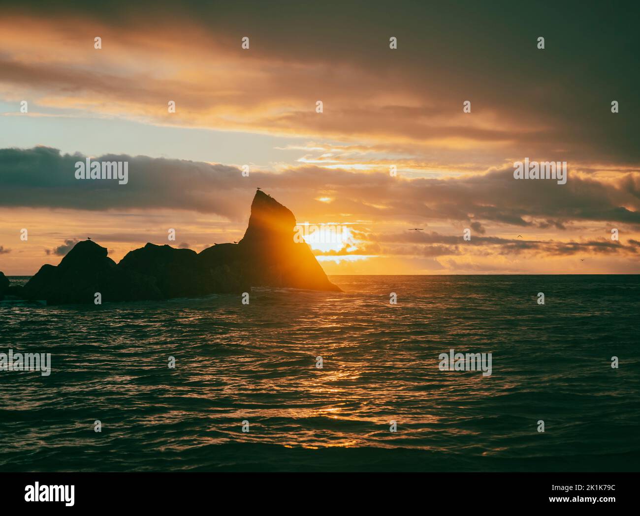 Sunset over the Atlantic Ocean from the Portuguese Azores islands. A choppy coast line during sunset featuring rocky outcrops and an amazing sunset. Stock Photo