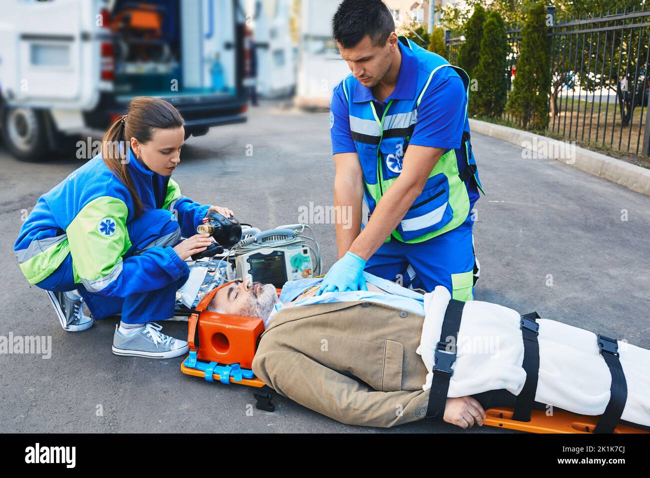 EMS paramedics performing closed-chest cardiac massage and artificial respiration for injured mature man who lies unconscious on medical stretcher nea Stock Photo