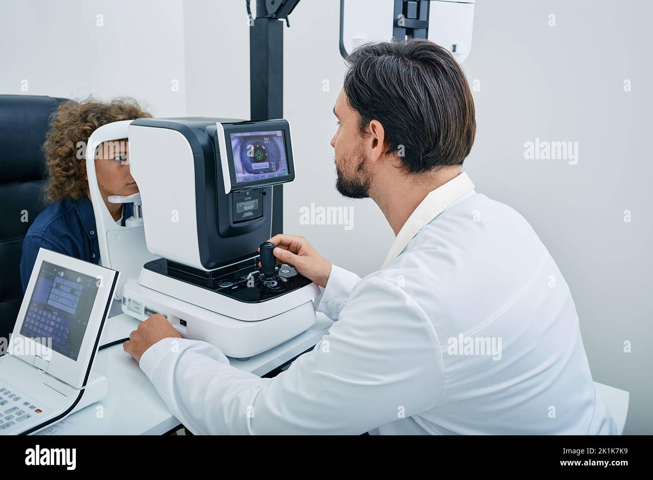 Optometrist using autorefractor determining required level of vision correction and determining individual's prescription for glasses for male child Stock Photo