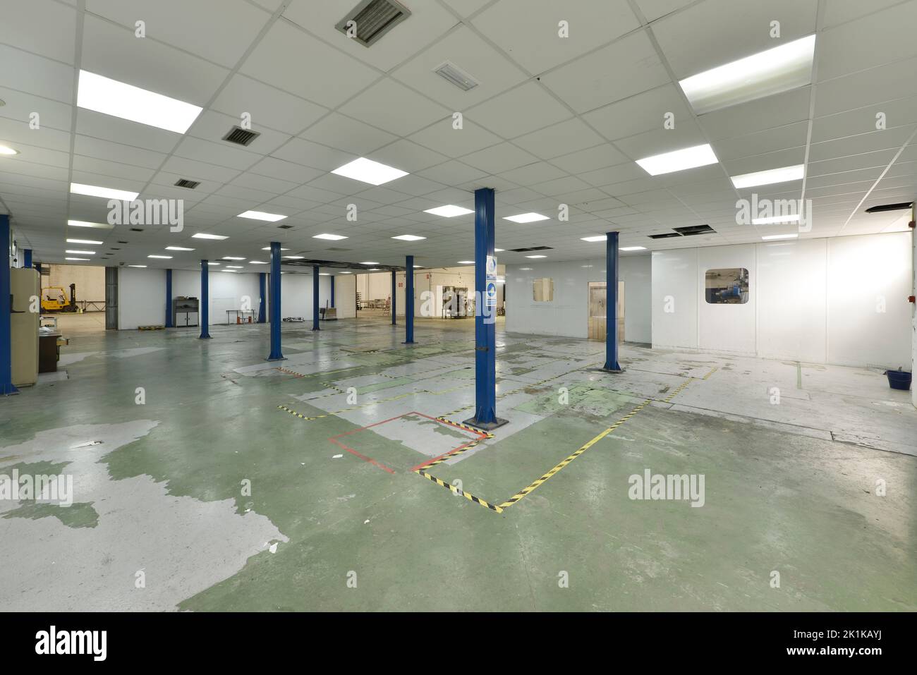 Empty industrial warehouse with blue metal columns, floors with green non-slip paint and technical ceilings with plasterboard ceilings Stock Photo