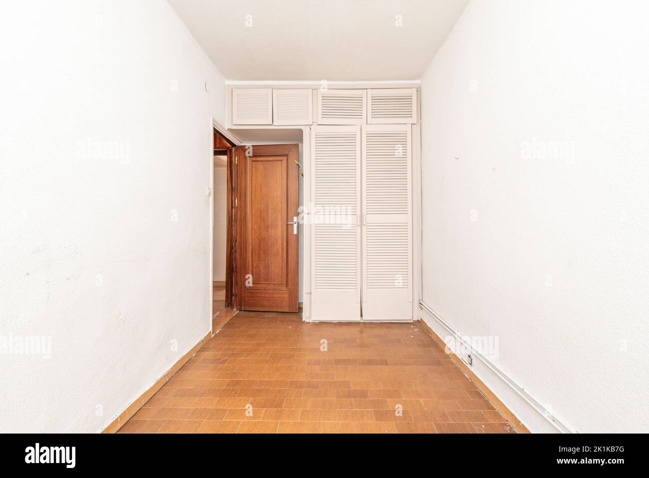 Small empty bedroom with white fitted wardrobe with Venetian style doors Stock Photo