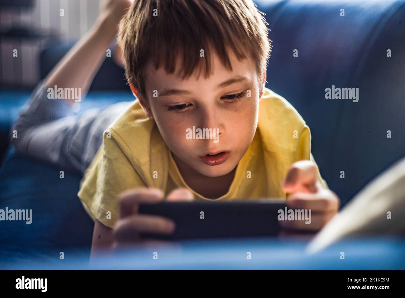 Boy lying on his front a sofa using a mobile phone Stock Photo