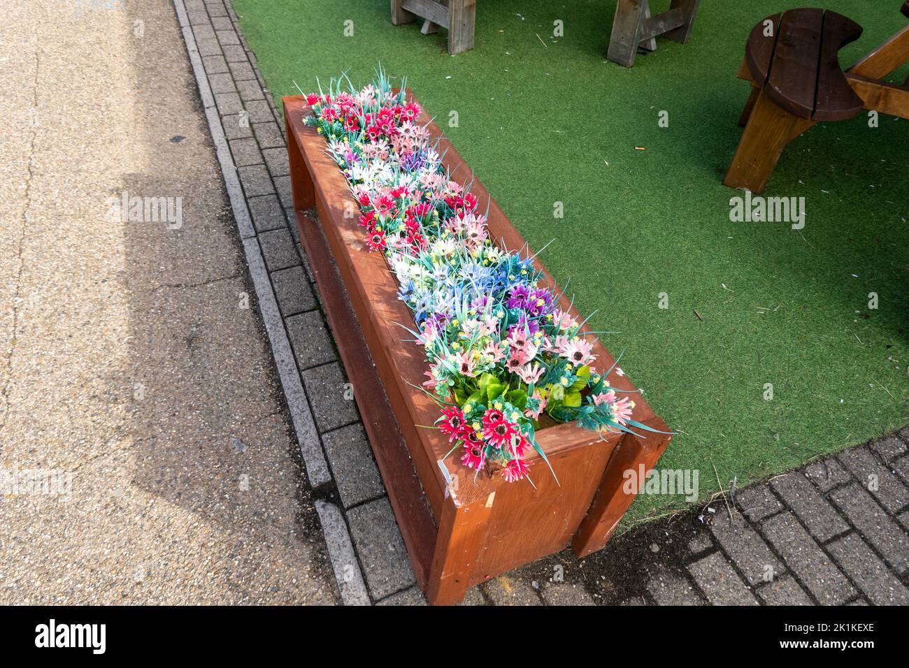 Raised wooden bed with plastic flowers made to look like real flowers in summertime Stock Photo